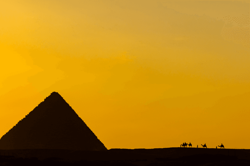 Camel riders at sunset at the Pyramids of Giza