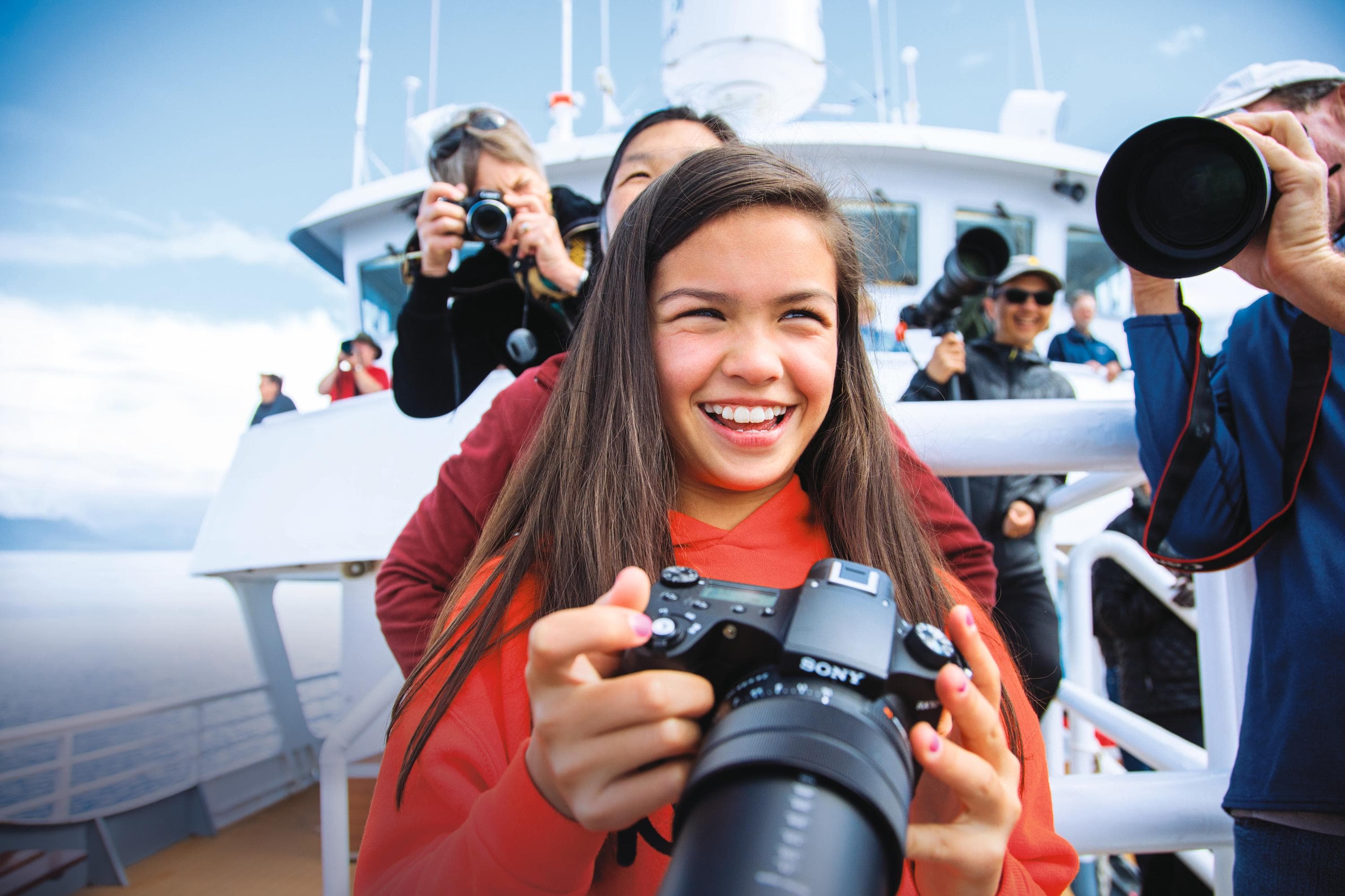 A young guest photographs whales bubble-net feeding from the ships bow, Southeast Alaska, USA