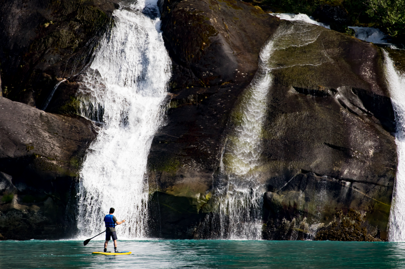 A guest explores Cascade Falls by standup paddle board in Tracy Arm, Alaska