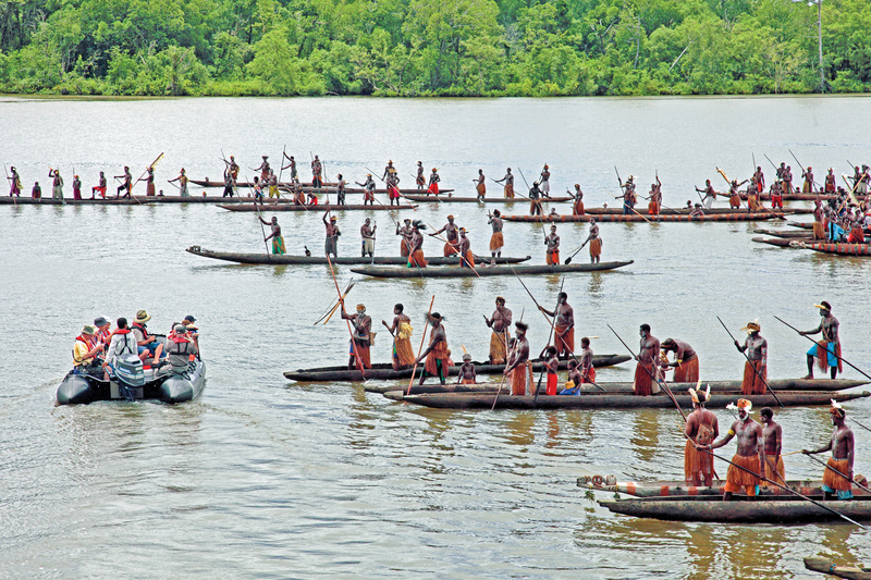Asmat Melanesian men in traditional decoration, paddling dug-out canoes, to greet guest on zodac in Syuru, western Papua.