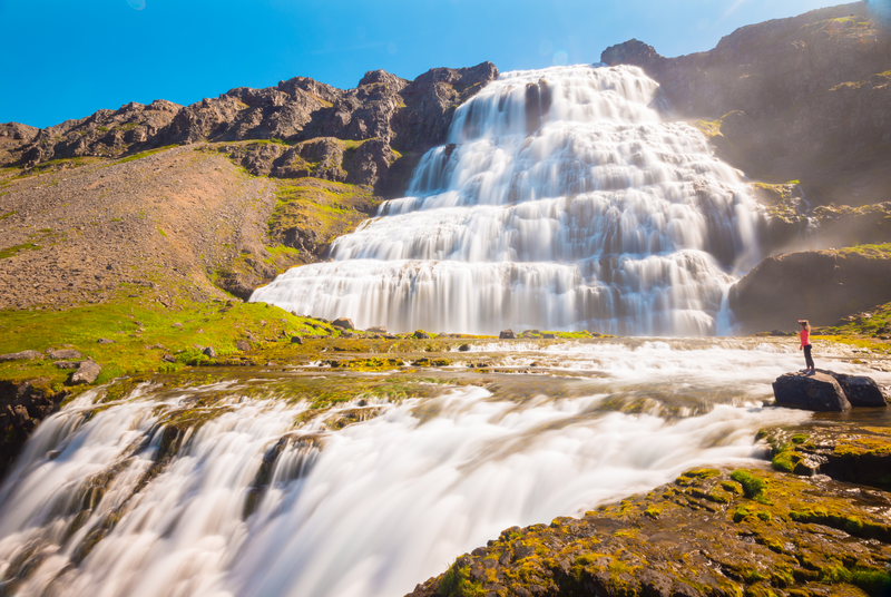 A hiker stands at the Dynjandi Waterfall in Westfjords, Iceland