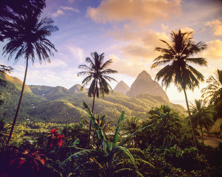 The sun sets over the Pitons as they tower above the Caribbean island of St Lucia and tropical foliage blankets the landscape