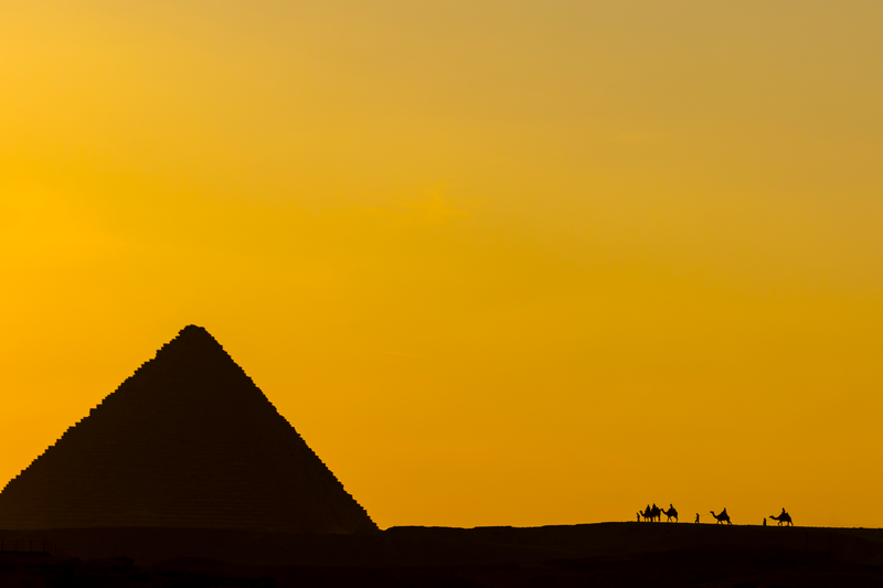 Camel riders at sunset at the Pyramids of Giza