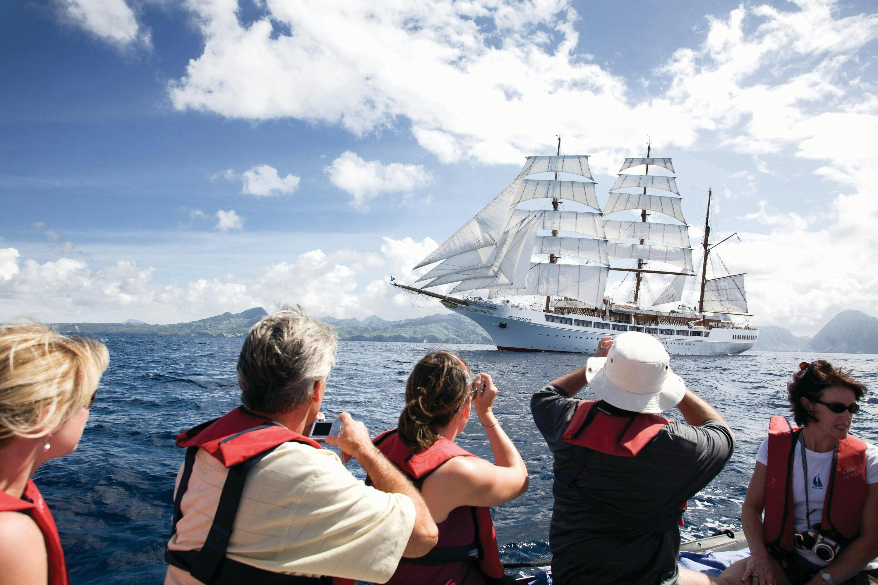 Guests enjoy the view of the ship Sea Cloud II in full sail from a watercraft expedition.