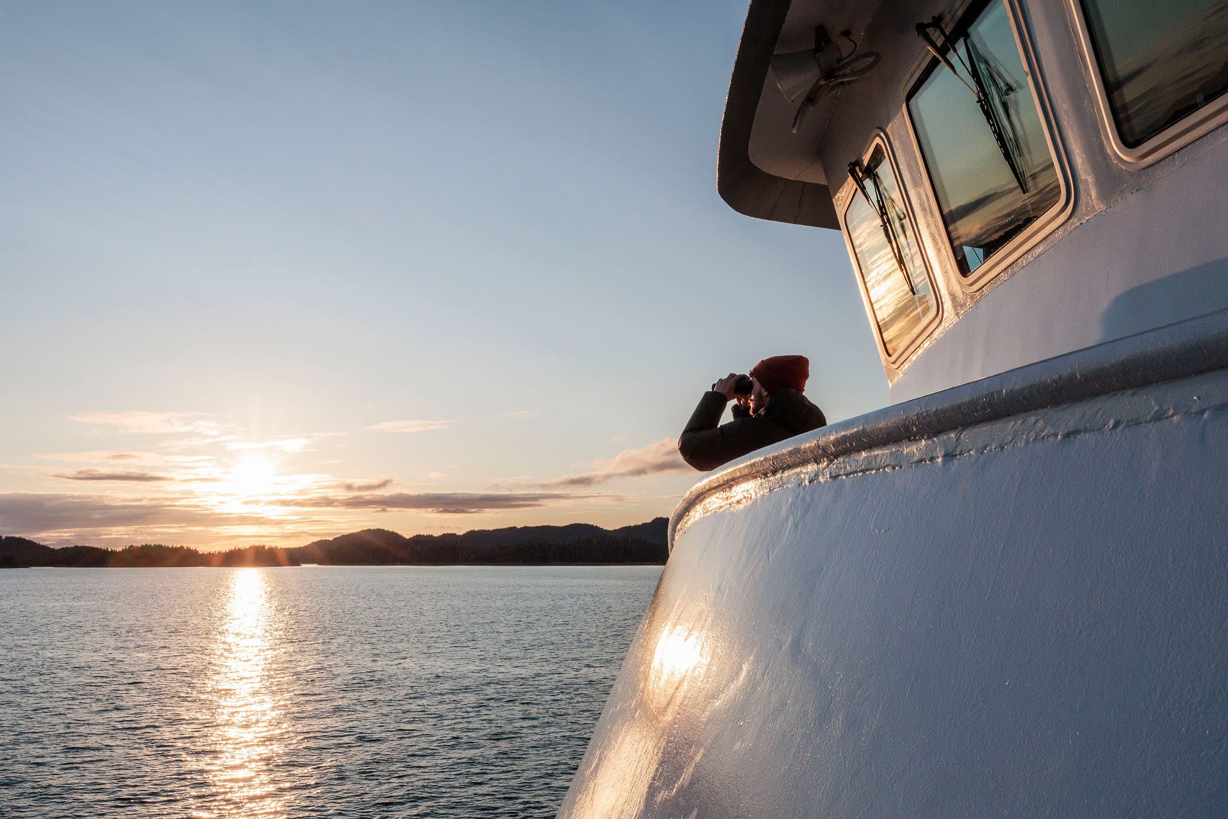 a man leans over the deck of a ship at sunset