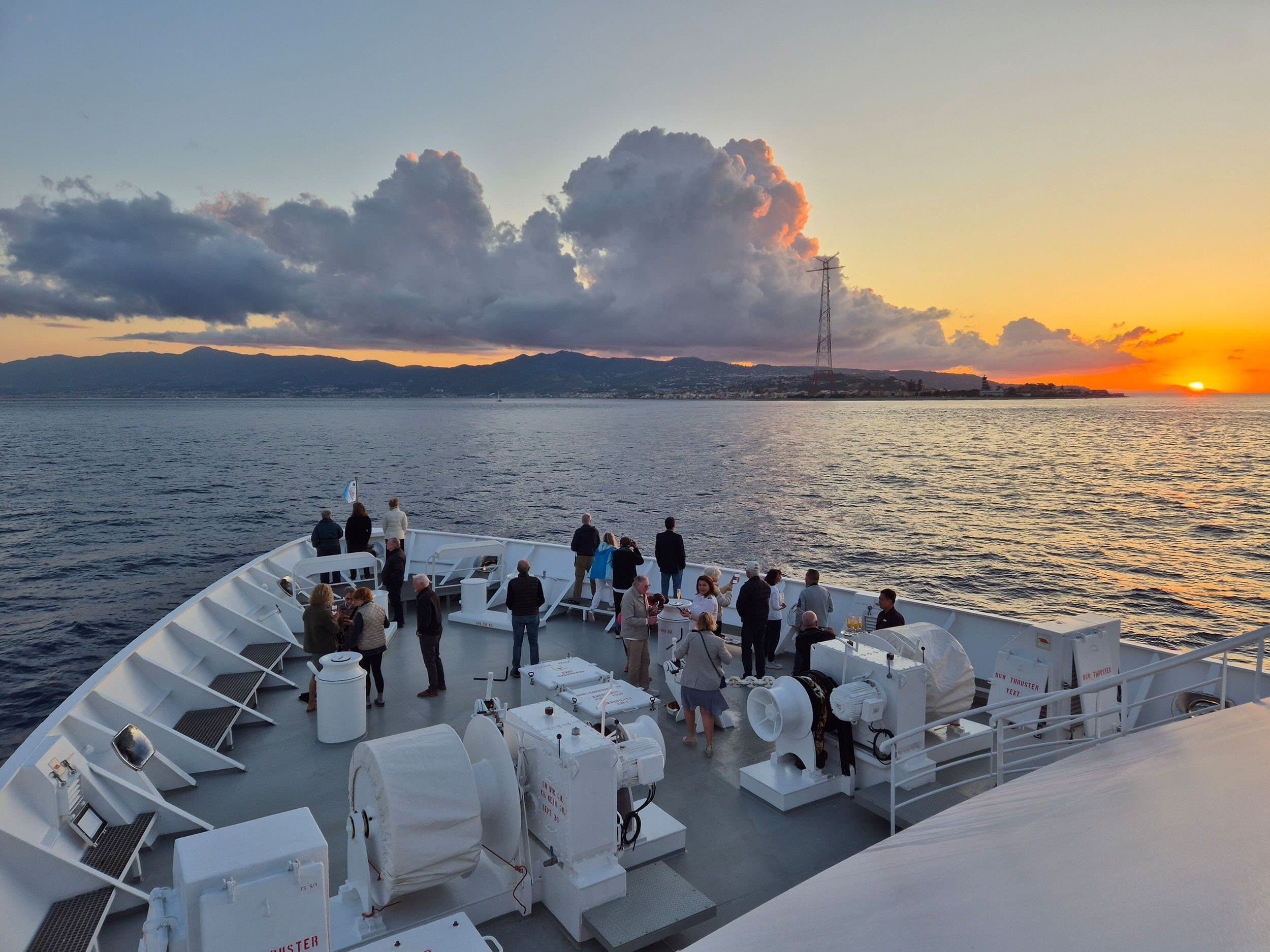 people stand on the bow of a ship at sunset