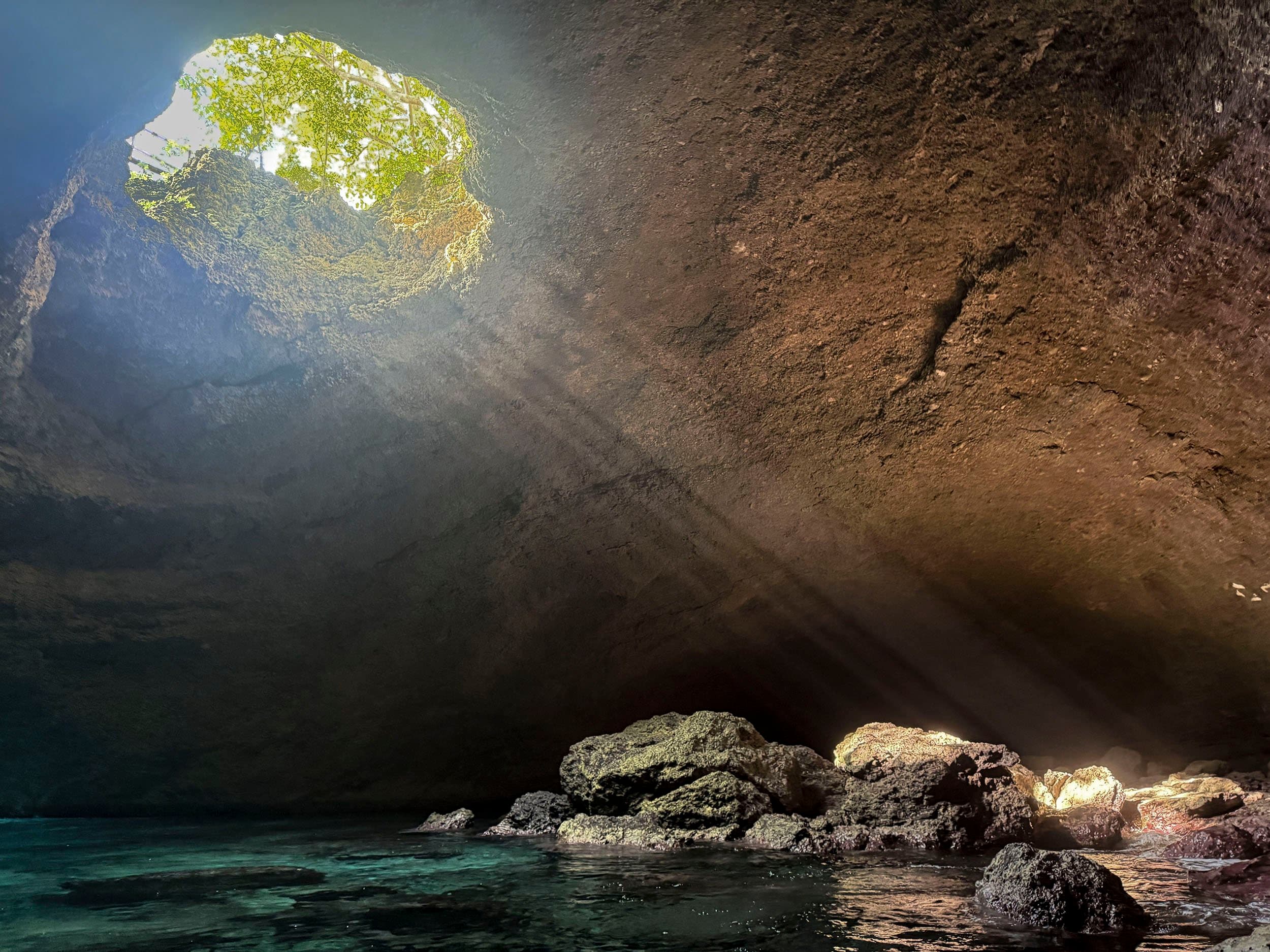 a cave with a large hole near the ceiling casting rays of sunlight
