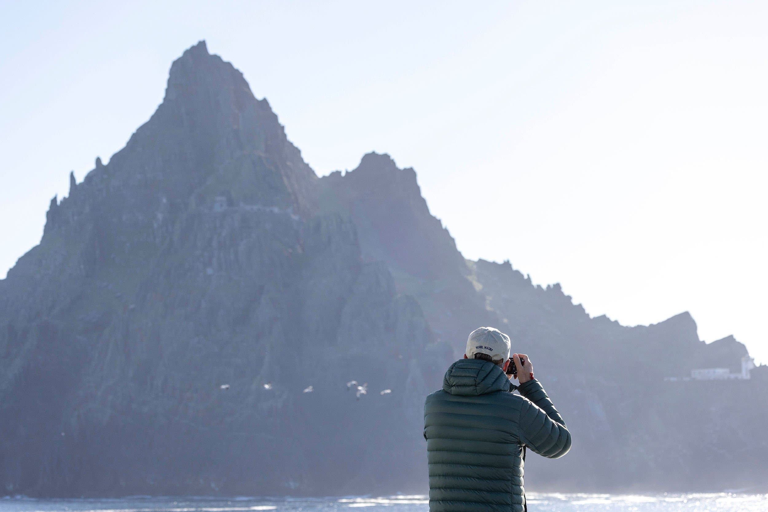 a man takes a photo of a jagged, rocky cliff