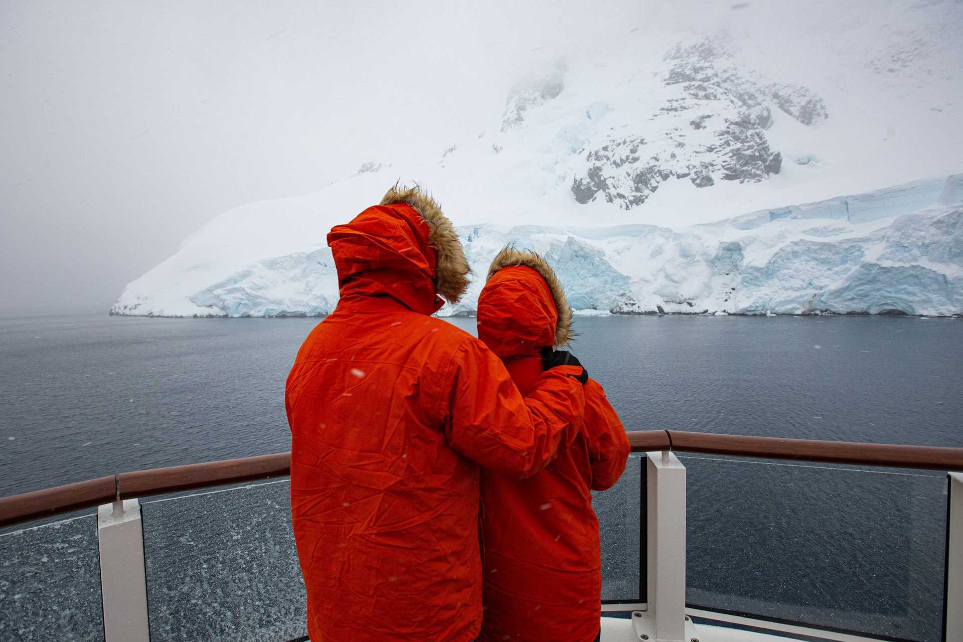 couple in parkas embracing while looking at icebergs in Antarctica