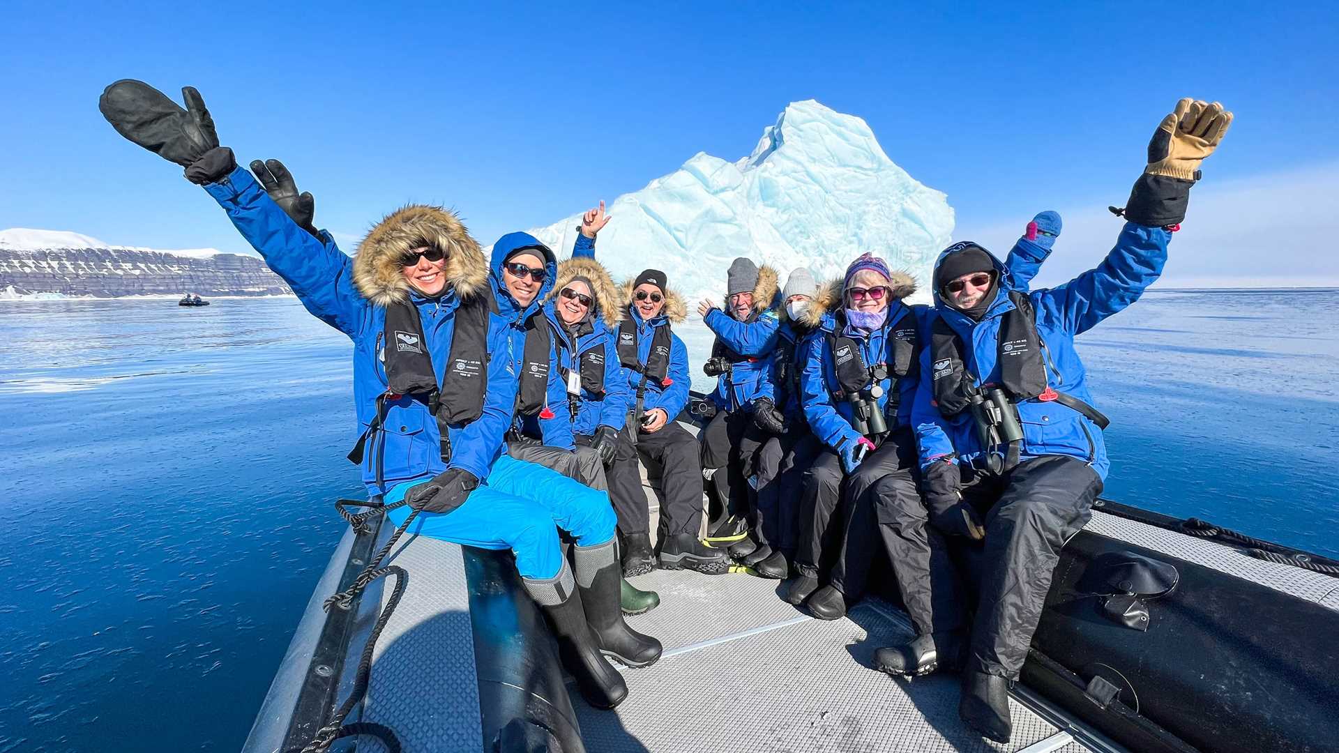 Guests in blue parkas sit in a Zodiac craft