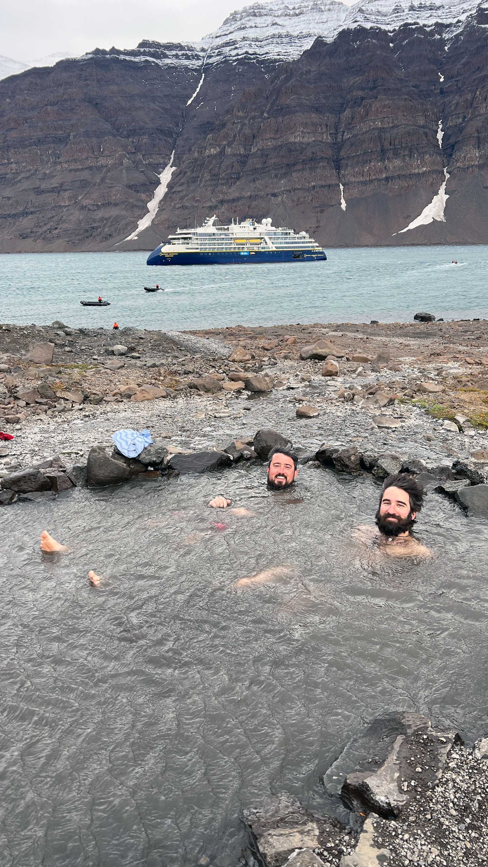 two men in a hot spring with ship in the background