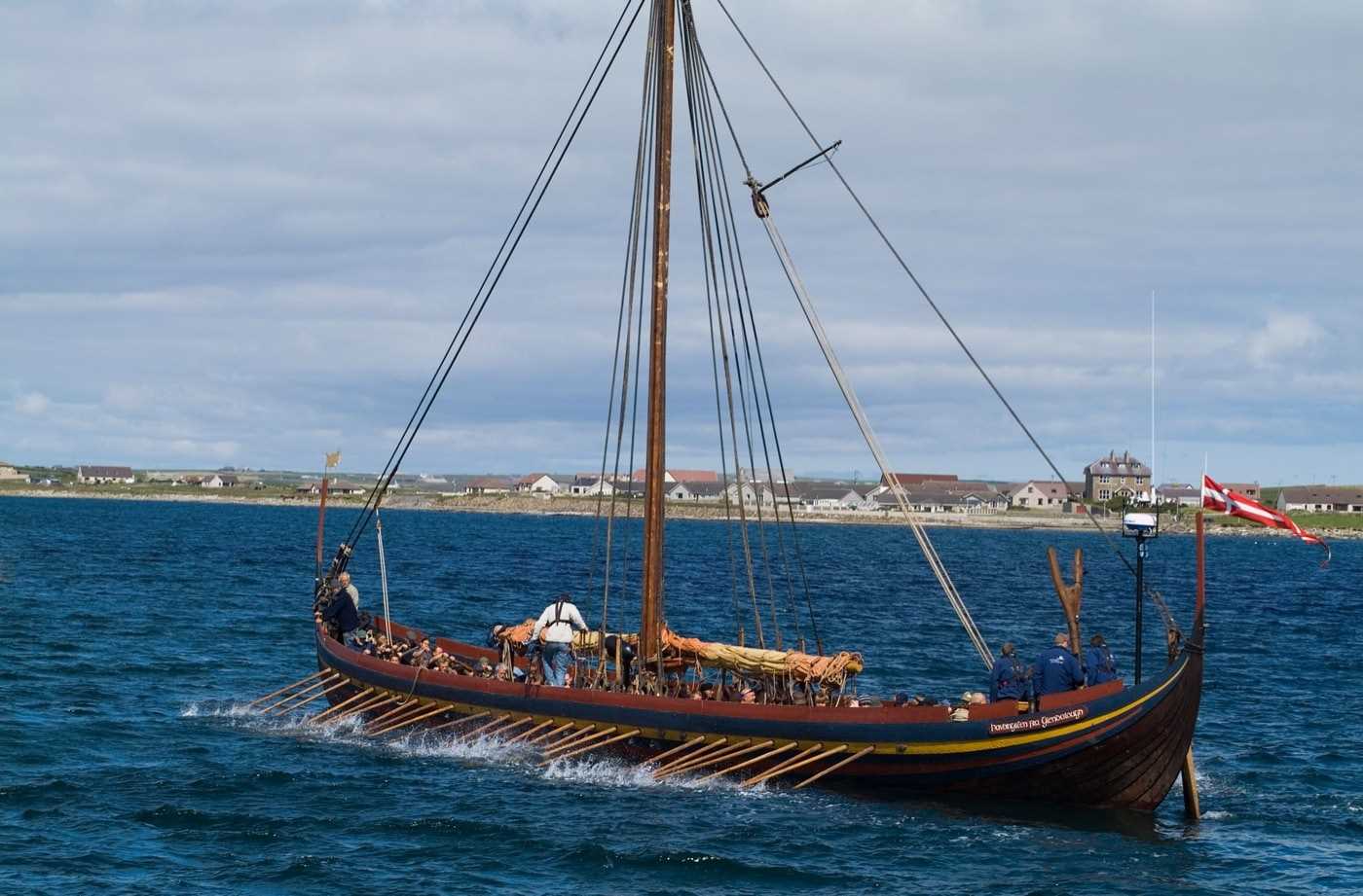 A viking longship in action, manned by a full crew of rowers and flying the flag of Denmark
