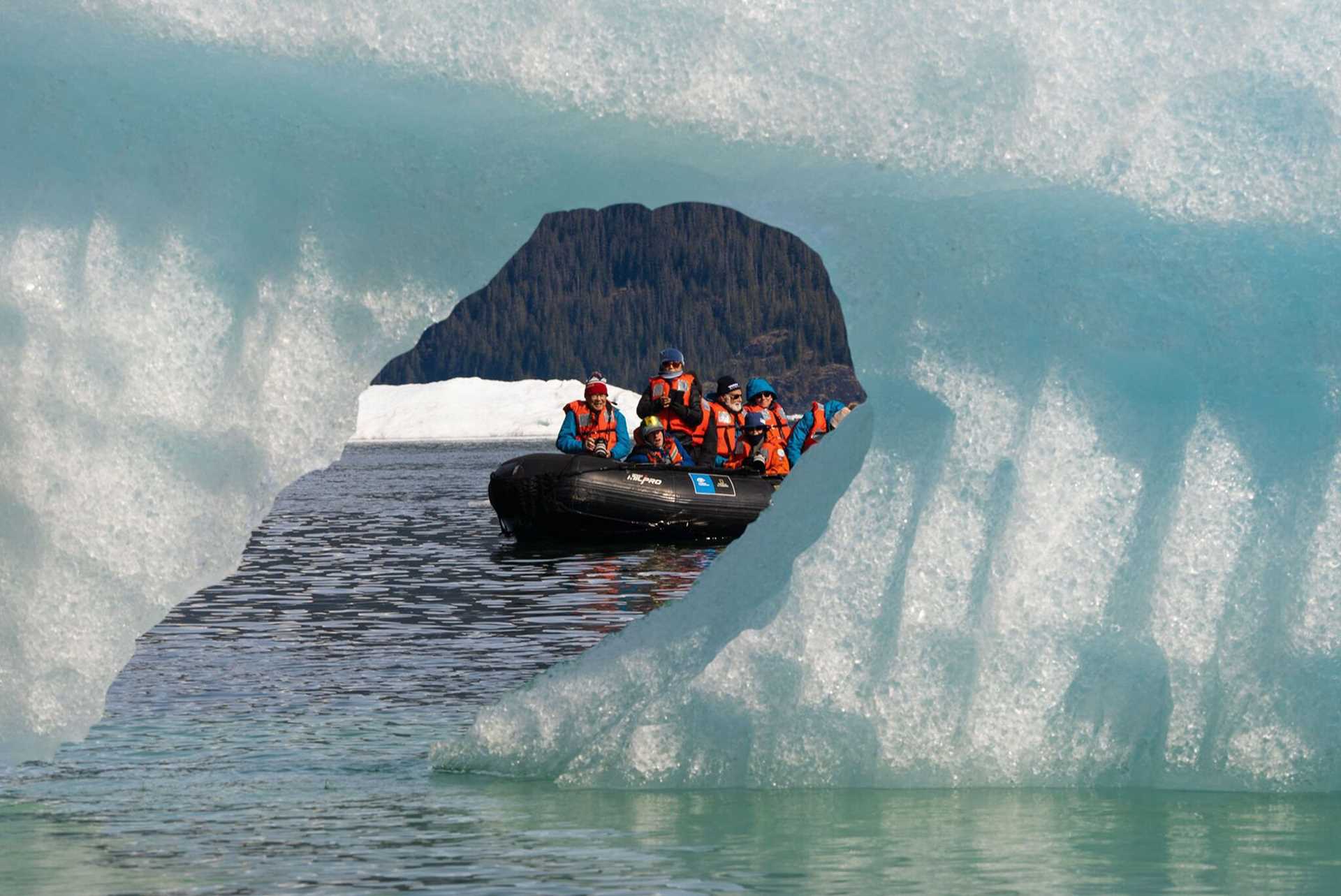 people in a zodiac behind an iceberg