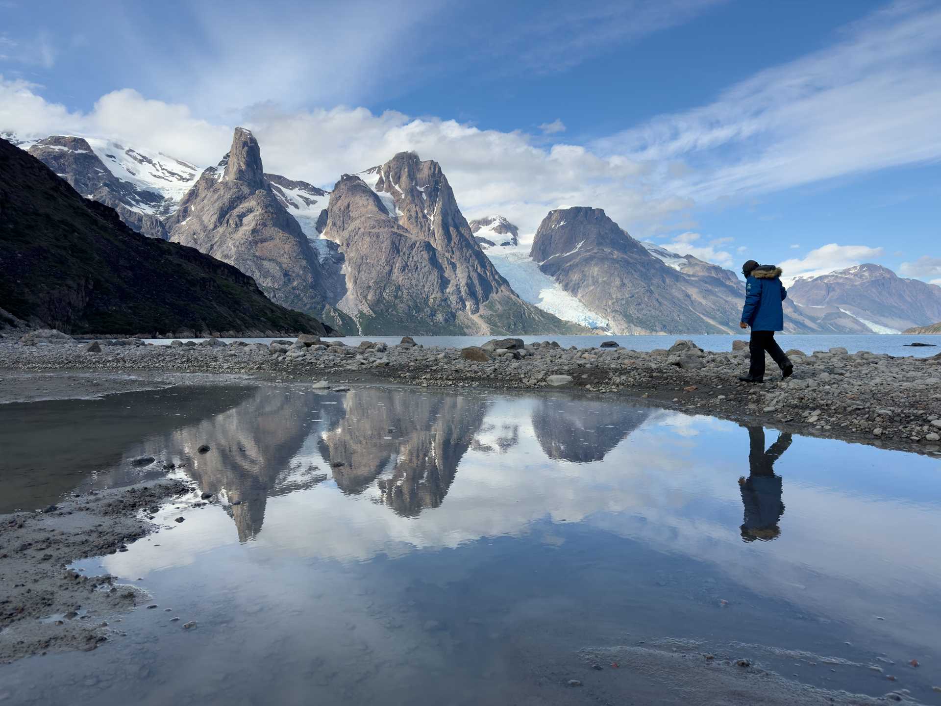 a person walks in front of mountains. the person and mountains are reflected in water below them
