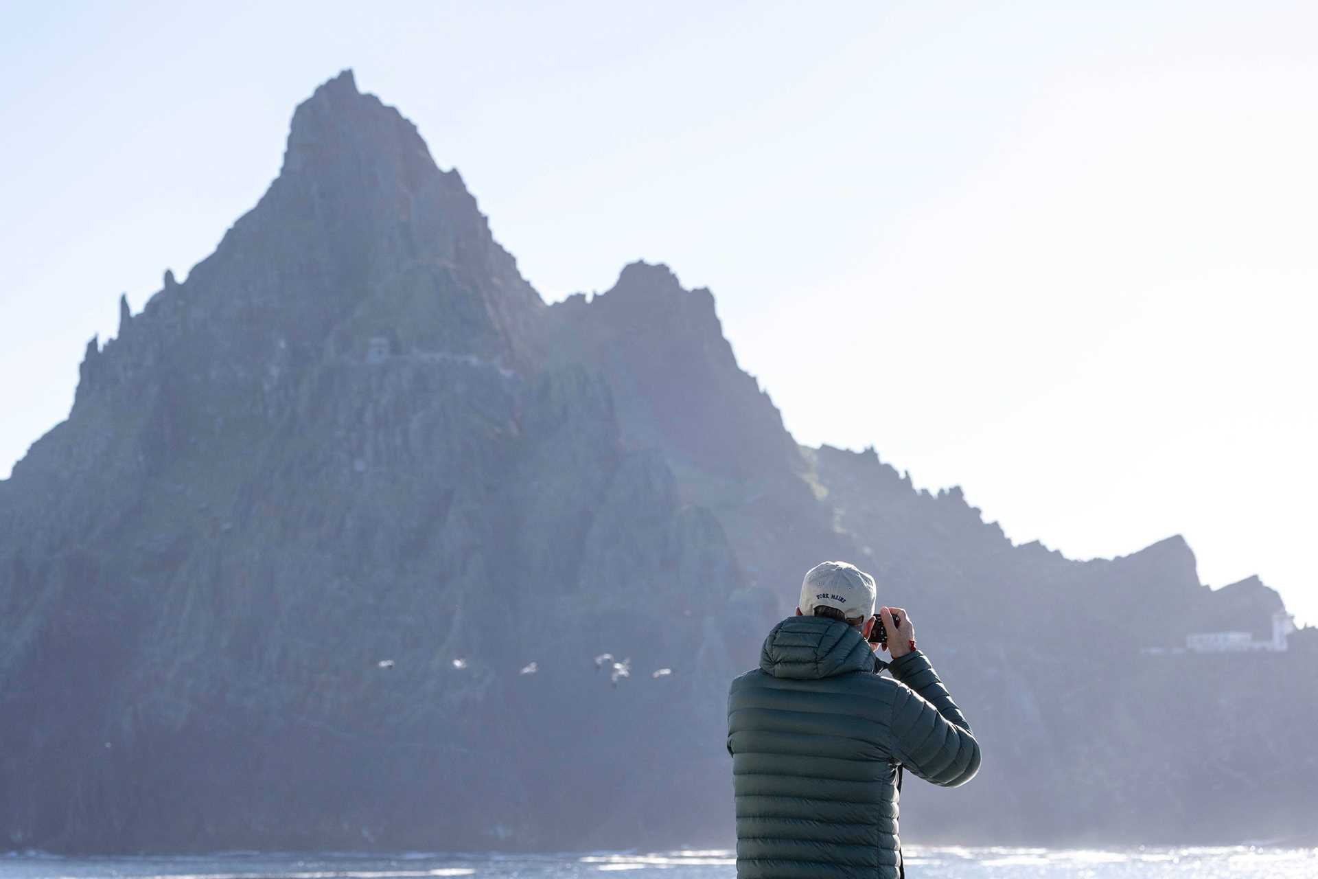 a man takes a photo of a jagged, rocky cliff