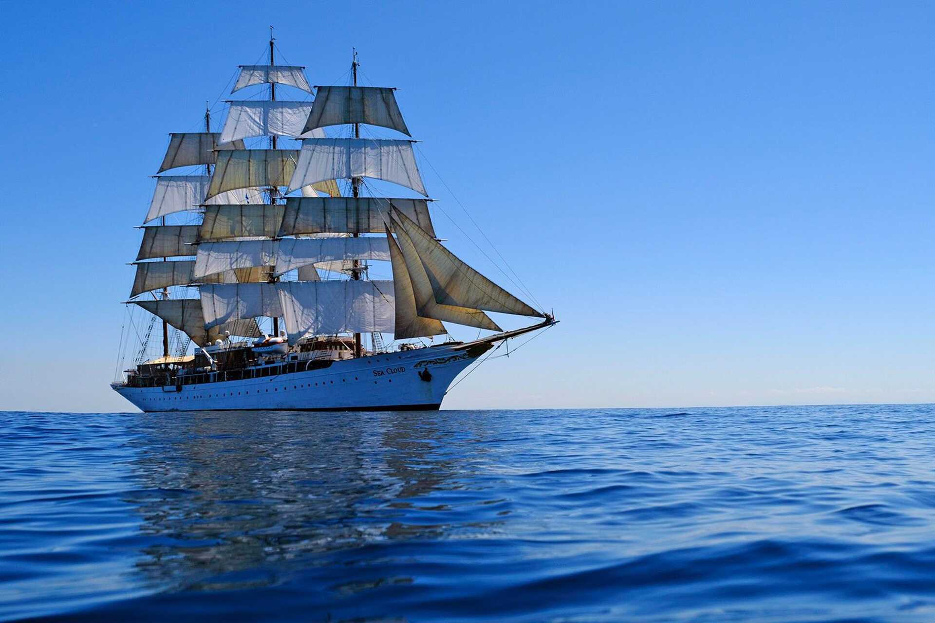 a tall-masted sailing ship against blue sky and smooth water