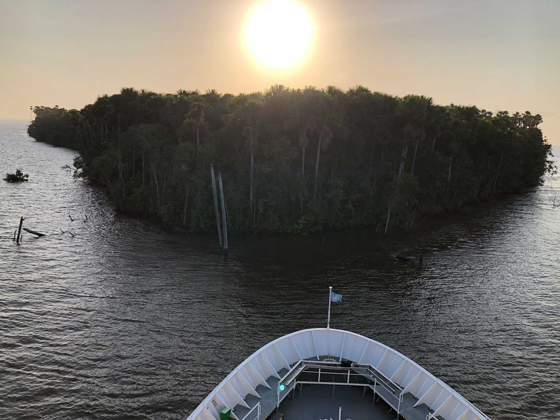 bow of national geographic explorer with lush green island behind it